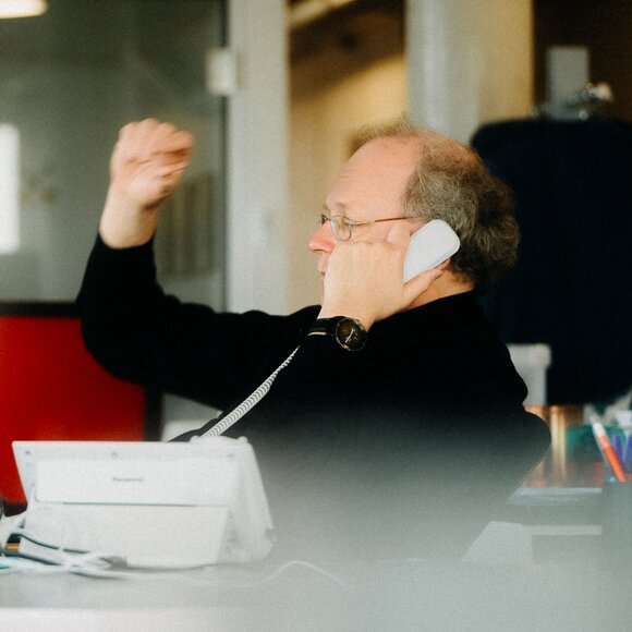 Berufstätiger Mann in einem dunklen Pullover telefoniert und gestikuliert mit seiner Hand. | © Photo: Ilja Kagan, 2022