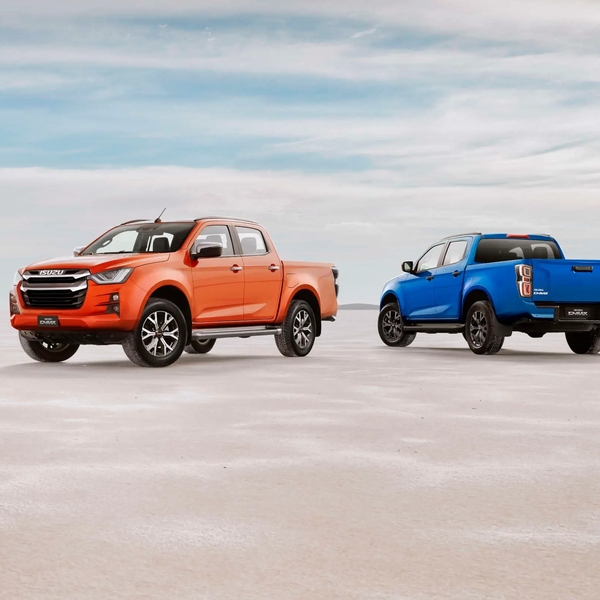 Two ISUZU D-MAX pickup trucks, one orange and one blue, parked side by side in the desert. | © ISUZU