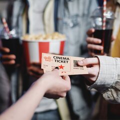 Hand holding a cinema ticket with popcorn and a soda in the background. | © Photo: @pressmaster / Freepik Licence