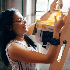 Dame steht vor einem Holz-Gestell, an dem Produktproben hängen