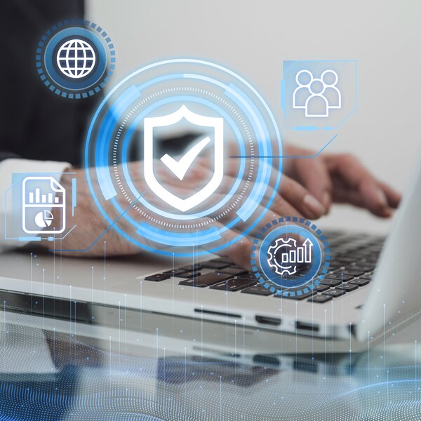 Person tippt auf Laptop, umgeben von digitalen Sicherheits-Icons: Schutzschild mit Häkchen, Globus, Nutzergruppe, Diagramm-Dokument und Zahnrad mit Statistik.