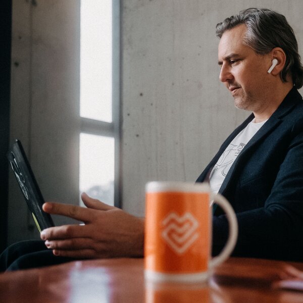 Man in a blazer using a tablet with wireless earbuds in a modern workspace. | © Photo: Ilja Kagan, 2022