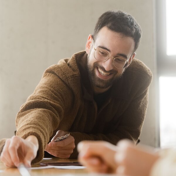 Smiling young man with glasses playing a board game and reaching out. | © Photo: Ilja Kagan, 2022