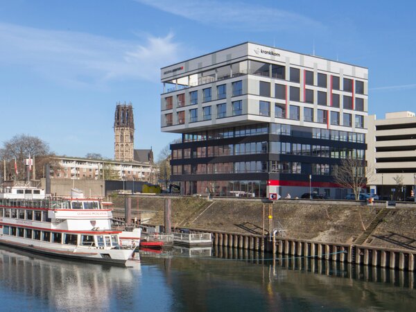 Krankikom GmbH office building at the Duisburg Inner Harbor with a sightseeing boat docked nearby. | © Krankikom GmbH, Photo: Alexander Kranki