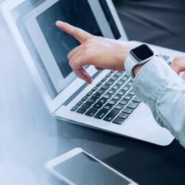 Close-up of a person's hand pointing at a laptop screen, wearing a smartwatch