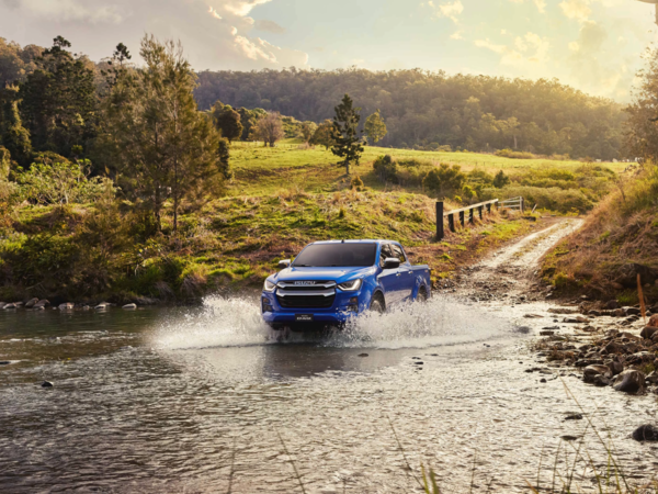 Blauer ISUZU D-MAX Pickup fährt durch einen flachen Bach in einer ländlichen, grünen Landschaft. | © ISUZU