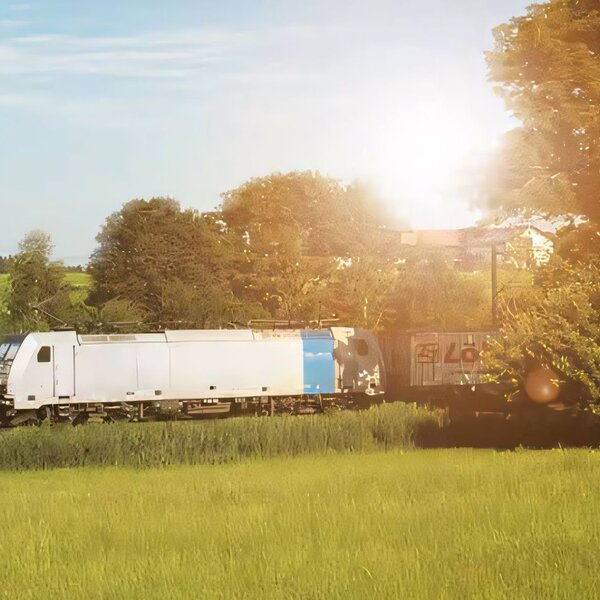 Ein Güterzug mit dem Kombiverkehr Logo transportiert Container durch eine helle grüne Landschaft bei strahlendem Sonnenschein
