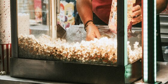 Eine Frau füllt Popcorn in eine Maschine. | © Photo: Unsplash Photocommunity, free image / Alex Kalligas @alexkall