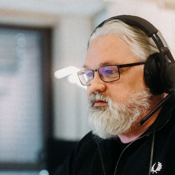 Ein Mann mit Bart und Brille arbeitet in einem Büro an einem Computer und trägt Kopfhörer. | © Photo: Ilja Kagan, 2022