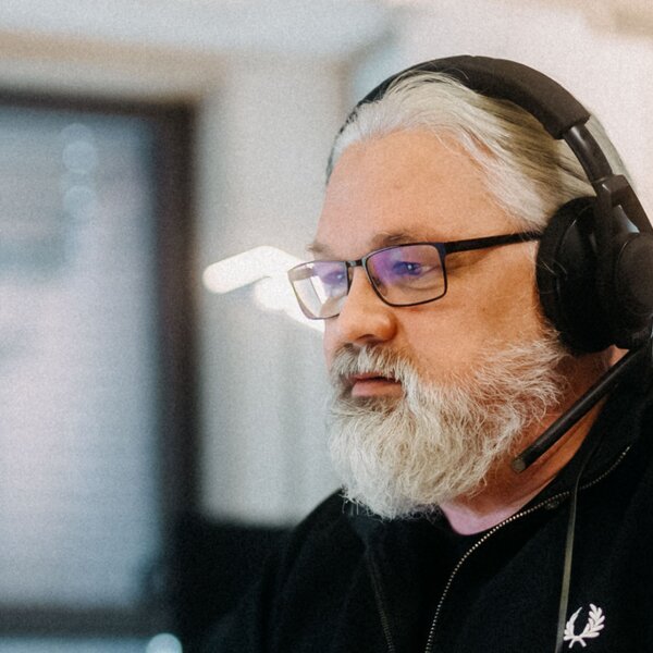 A man with a beard and glasses is working at a computer in an office and wearing headphones. | © Photo: Ilja Kagan, 2022