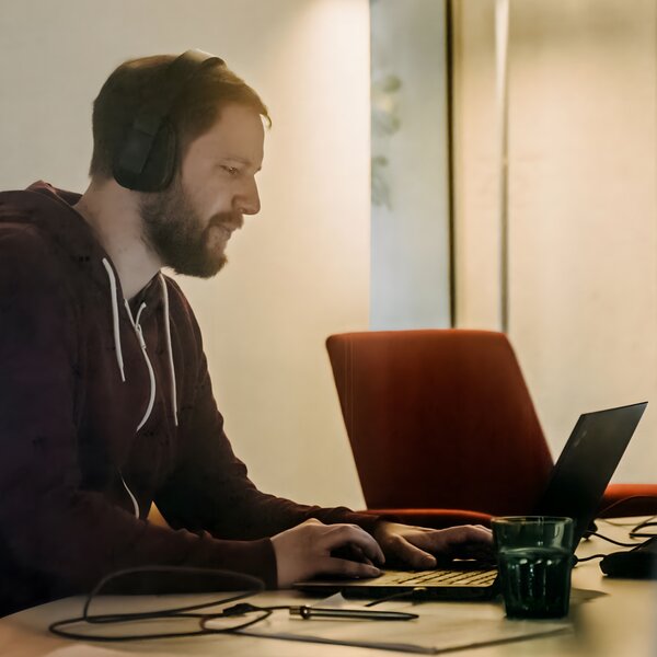 Konzentrierter Mann mit Kopfhörern arbeitet an einem Laptop am Schreibtisch. | © Photo: Ilja Kagan, 2022