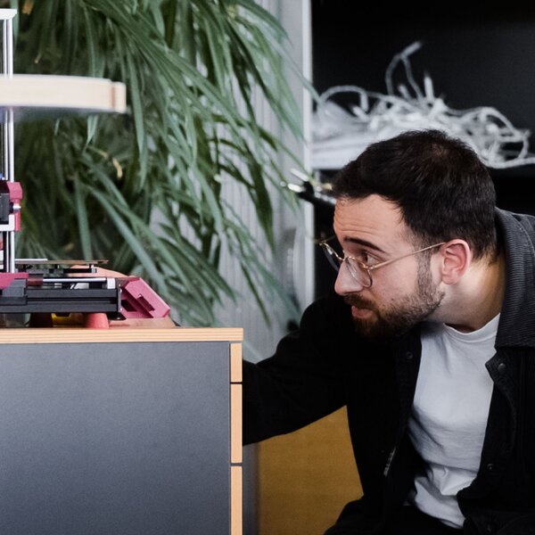 Technician inspecting 3D printer. | © Photo: Ilja Kagan, 2022 Man with glasses kneeling in front of a desk inspecting a 3D printer in the office. | © Photo: Ilja Kagan, 2022
