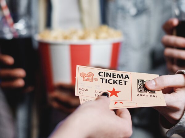 Hand hält ein Kinoticket mit Popcorn und einem Softdrink im Hintergrund. | © Photo: @pressmaster / Freepik Licence
