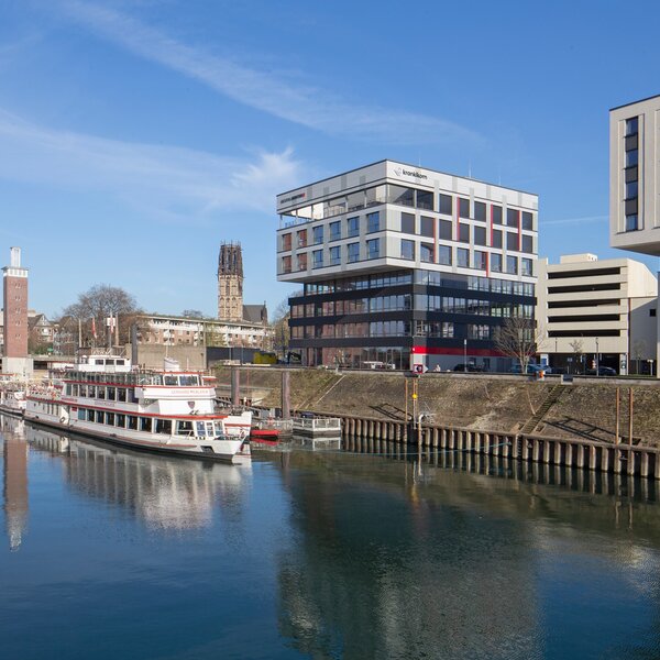 Krankikom GmbH office building at the Duisburg Inner Harbor with a sightseeing boat docked nearby. | © Krankikom GmbH, Photo: Alexander Kranki