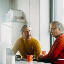 Zwei Männer sitzen an einem Tisch in einem Büro.