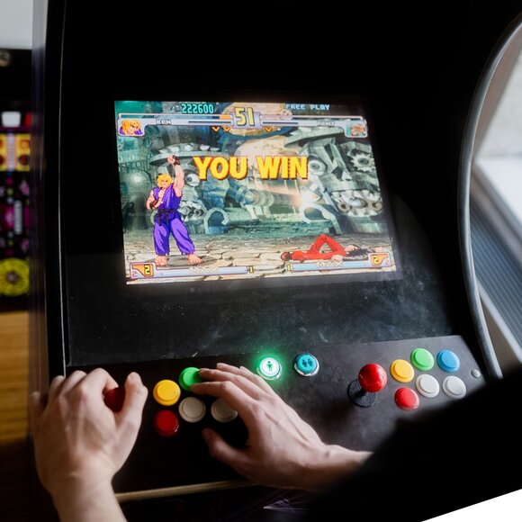 Hände einer Person, die ein klassisches Kampf-Arcade-Spiel spielt mit 'YOU WIN' auf dem Bildschirm. | © Photo: Ilja Kagan, 2022